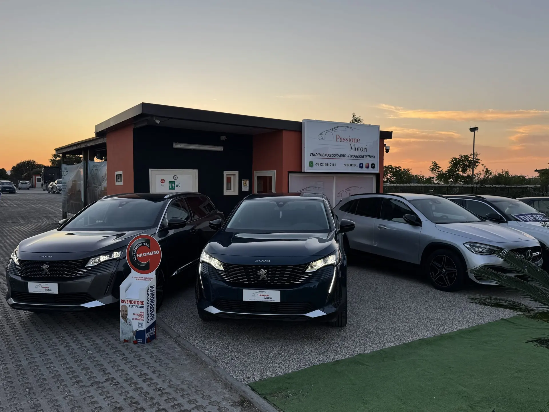 La sede di Passione Motori in Via Pomigliano a Sant'Anastasia al tramonto, con le vetture in esposizione davanti all'insegna